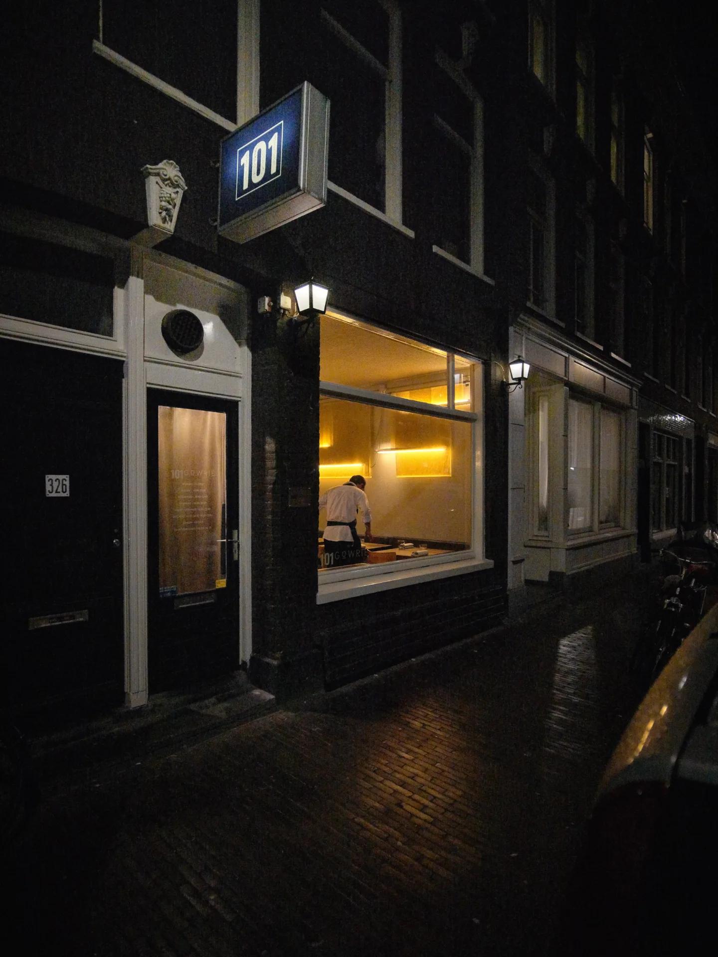 Gevel van restaurant 101 Gowrie aan de Govert Flinckstraat in Amsterdam bij avond, met zicht door het raam naar binnen