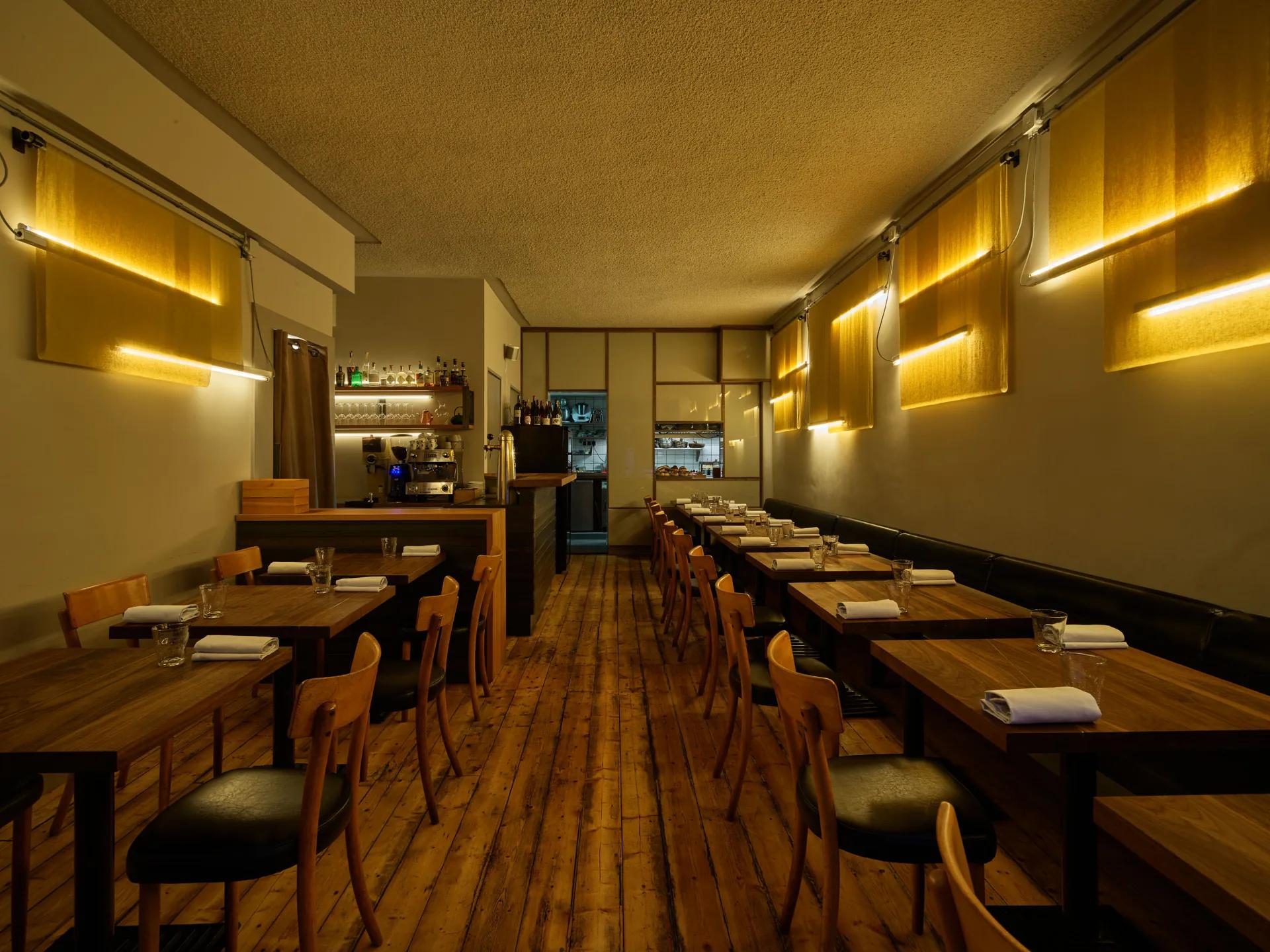 Akoestisch spuitwerk op het plafond van restaurant 101 Gowrie in Amsterdam, boven houten tafels en verlichte wandpanelen